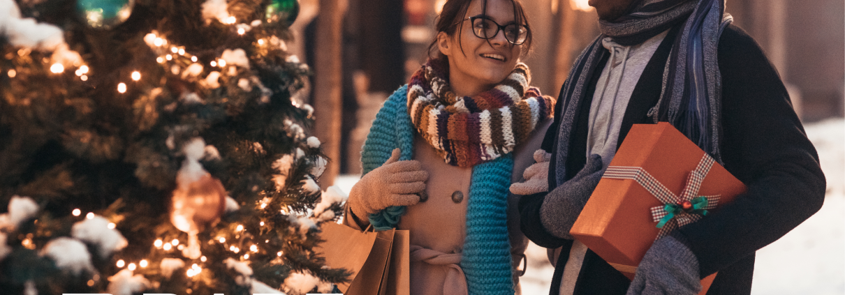 A man and woman holding presents and shopping bags standing beside a Christmas tree