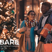 A man and woman holding presents and shopping bags standing beside a Christmas tree