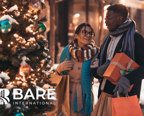 A man and woman holding presents and shopping bags standing beside a Christmas tree