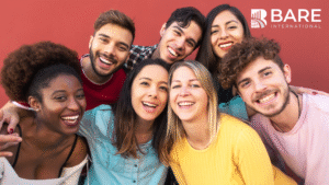 Group of seven smiling, happy individuals against a red background.